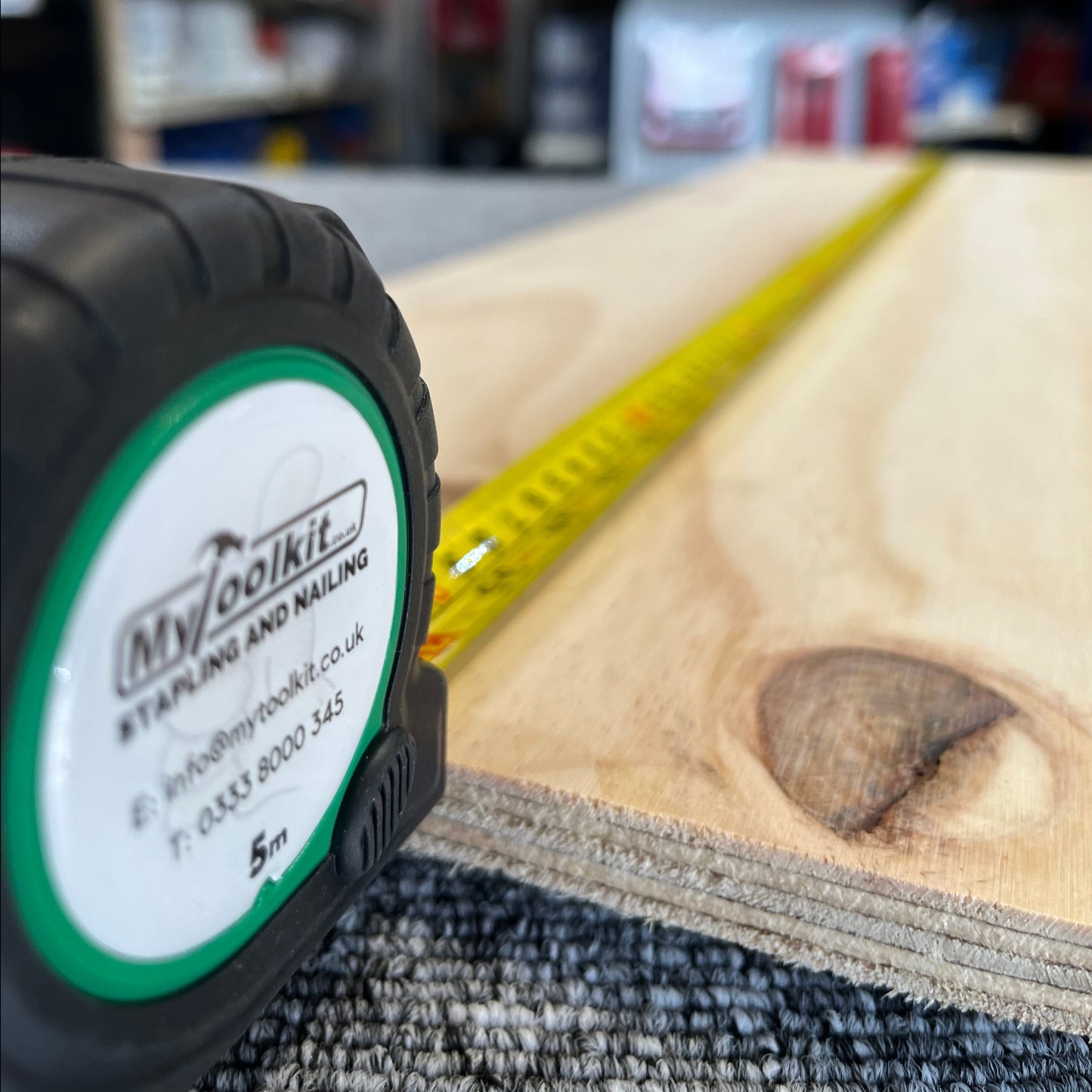 A green MyToolkit Stapling and Nailing tape measure with a yellow blade measuring a piece of timber